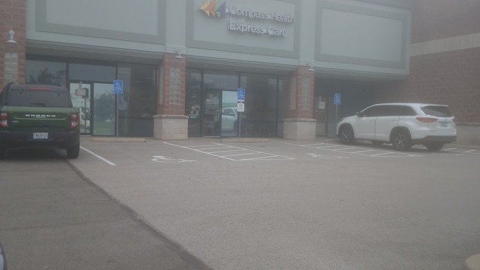 Exterior parking lot view showing Compass Health Express Care facility storefront with brick columns and parked vehicles