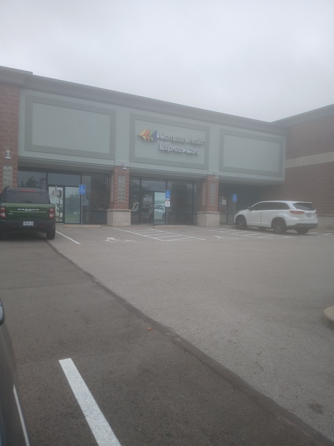 Exterior parking lot view showing Compass Health Express Care facility storefront with brick columns and parked vehicles
