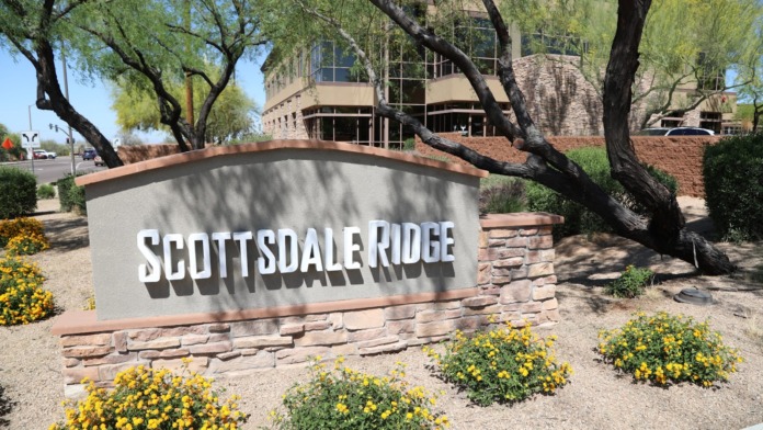 Exterior property sign reading Scottsdale Ridge with landscaped grounds, mature trees, and building facade.