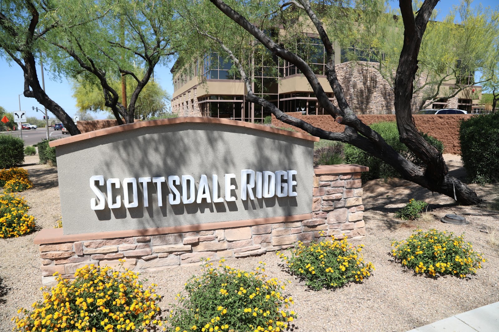 Exterior property sign reading Scottsdale Ridge with landscaped grounds, mature trees, and building facade.