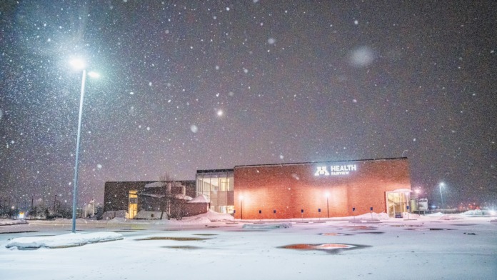 Exterior nighttime view of healthcare facility with snow, illuminated signage, brick architecture, and winter landscaping