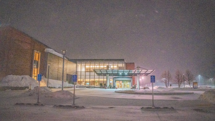 Exterior view of treatment facility in snowy winter evening showing brick and glass architecture, parking area, and landscaped surroundings