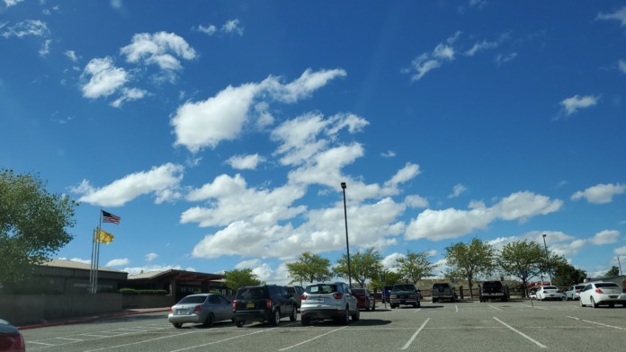 Exterior parking area with facility building, vehicles parked, landscaping, and clear blue sky