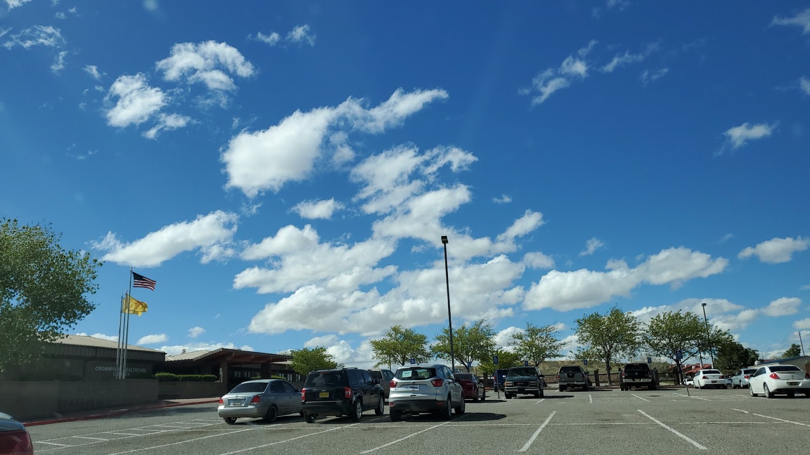 Exterior parking area with facility building, vehicles parked, landscaping, and clear blue sky