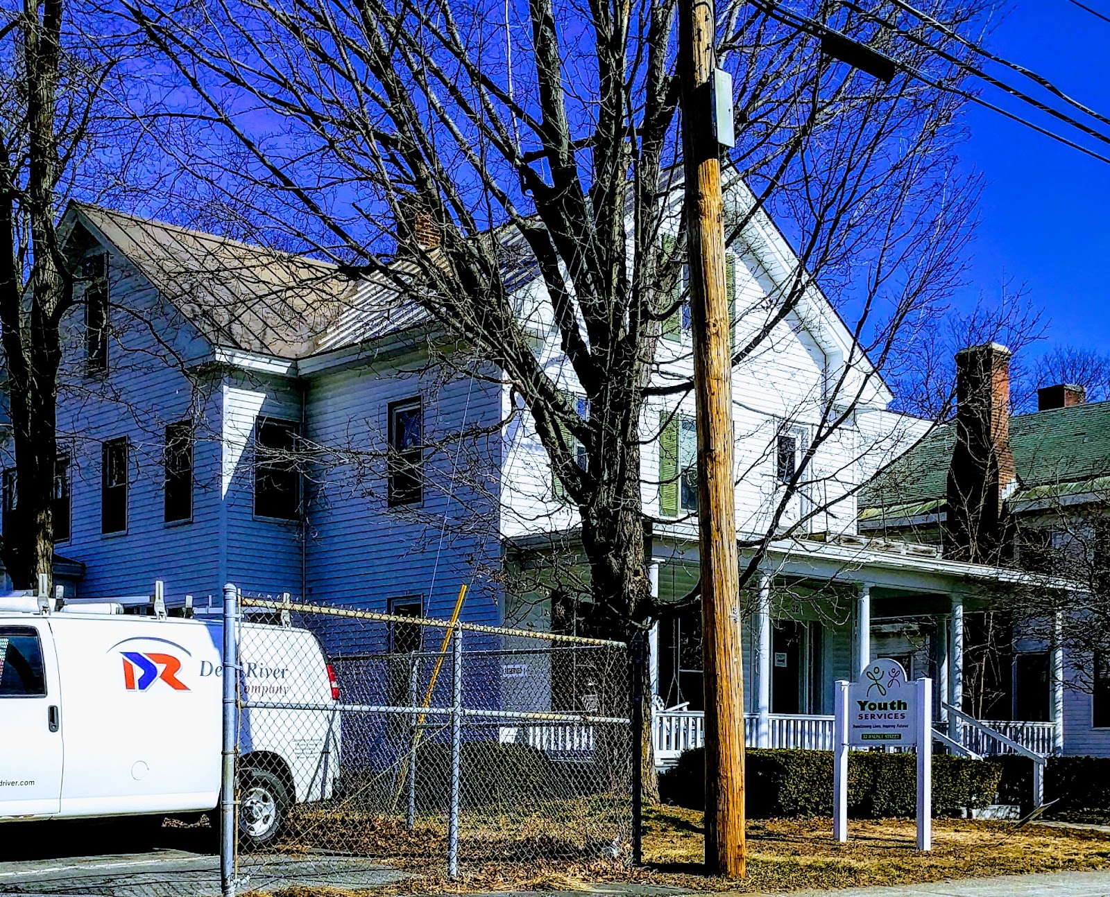 Exterior view of white and blue wooden buildings with front porch, fenced yard, and facility signage visible