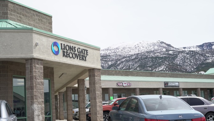Exterior showing stone facade, entrance signage, parking area, and snow-covered mountains in background