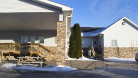 Exterior view of brick and siding treatment facility with wooden deck, picnic tables, and landscaping