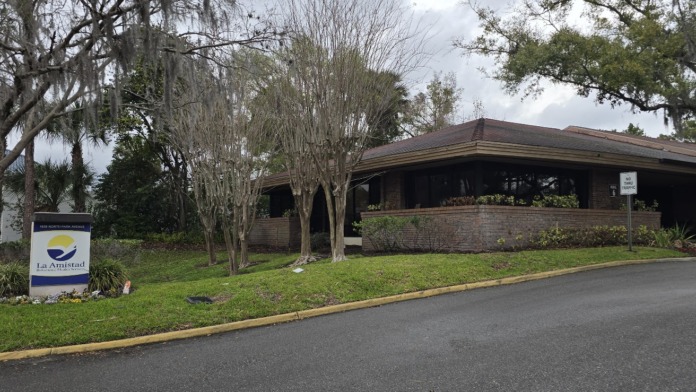Exterior view of treatment facility showing brick building, large windows, mature trees, and parking area entrance