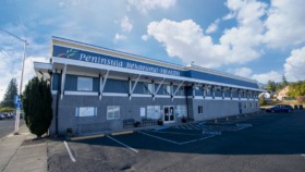 Exterior view of Peninsula Behavioral Health building showing blue roof, main signage, parking spaces with handicap access, and surrounding neighborhood