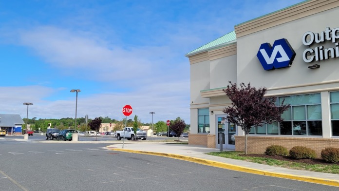Exterior view of VA Outpatient Clinic showing building facade, windows, landscaping, parking area with multiple vehicles