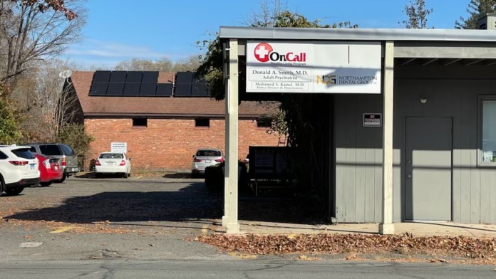 Exterior view of brick building with parking area, OnCall signage, and attached medical office structure with solar panels