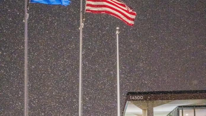 Exterior showing Minnesota and American flags displayed at facility entrance with snow, architectural pergola, and evening illumination