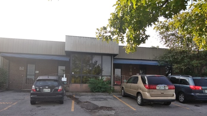 Exterior front entrance of brick building with parking area, vehicles parked, blue trim on windows and doors