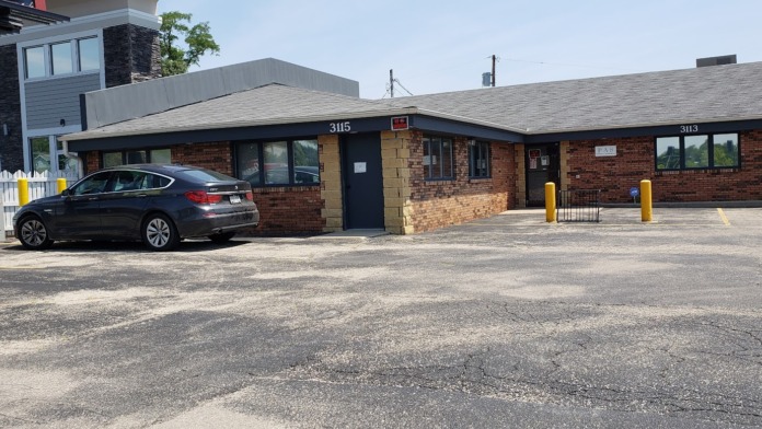 Exterior front entrance showing brick building with numbered units 3115 and 3113, parking area, and landscaping