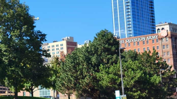 Outdoor grounds view showing green lawn, trees, and facility building with urban backdrop