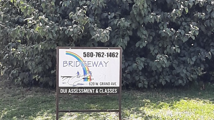 Outdoor signage displaying Bridgeway logo and DUI assessment services information with landscaped grounds and vegetation in background