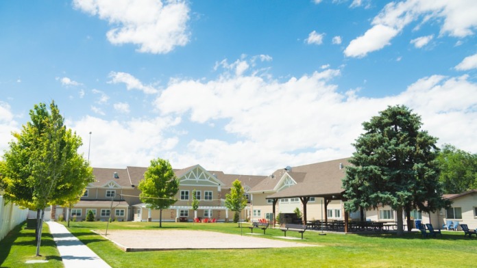 Exterior view showing manicured lawns, covered pavilion, mature trees, and multiple facility buildings in mountain setting