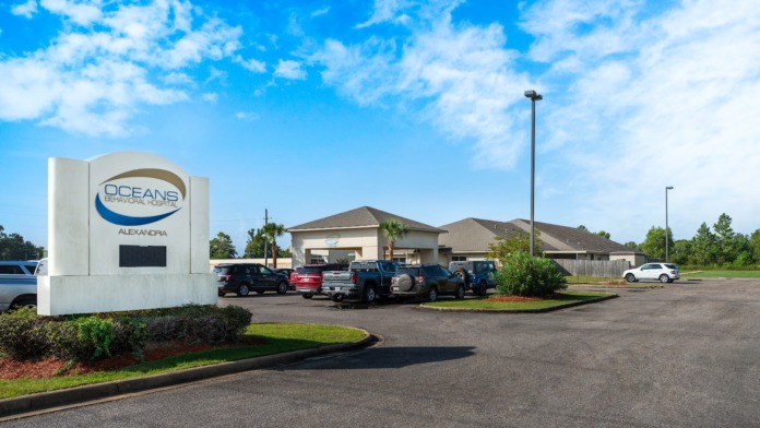 Exterior view showing facility parking lot with parked vehicles, main building structure, and landscaped grounds with sign