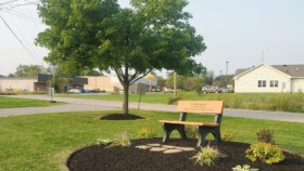 Exterior view of treatment facility grounds featuring a wooden memorial bench with landscaping and shade tree
