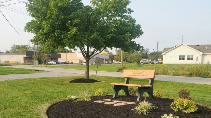 Exterior view of treatment facility grounds featuring a wooden memorial bench with landscaping and shade tree