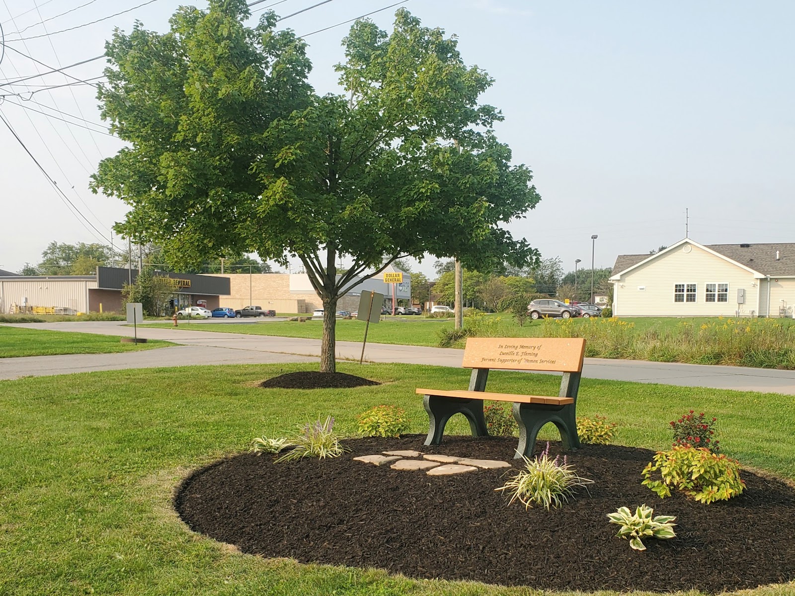 Exterior view of treatment facility grounds featuring a wooden memorial bench with landscaping and shade tree
