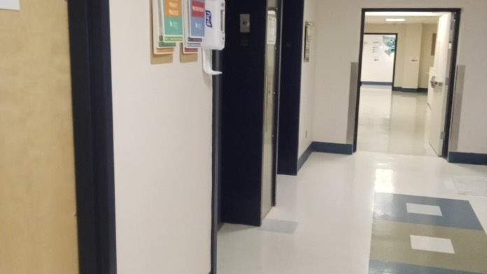 Interior hallway with clean floors, colored door frames, exit signage, and directional information boards