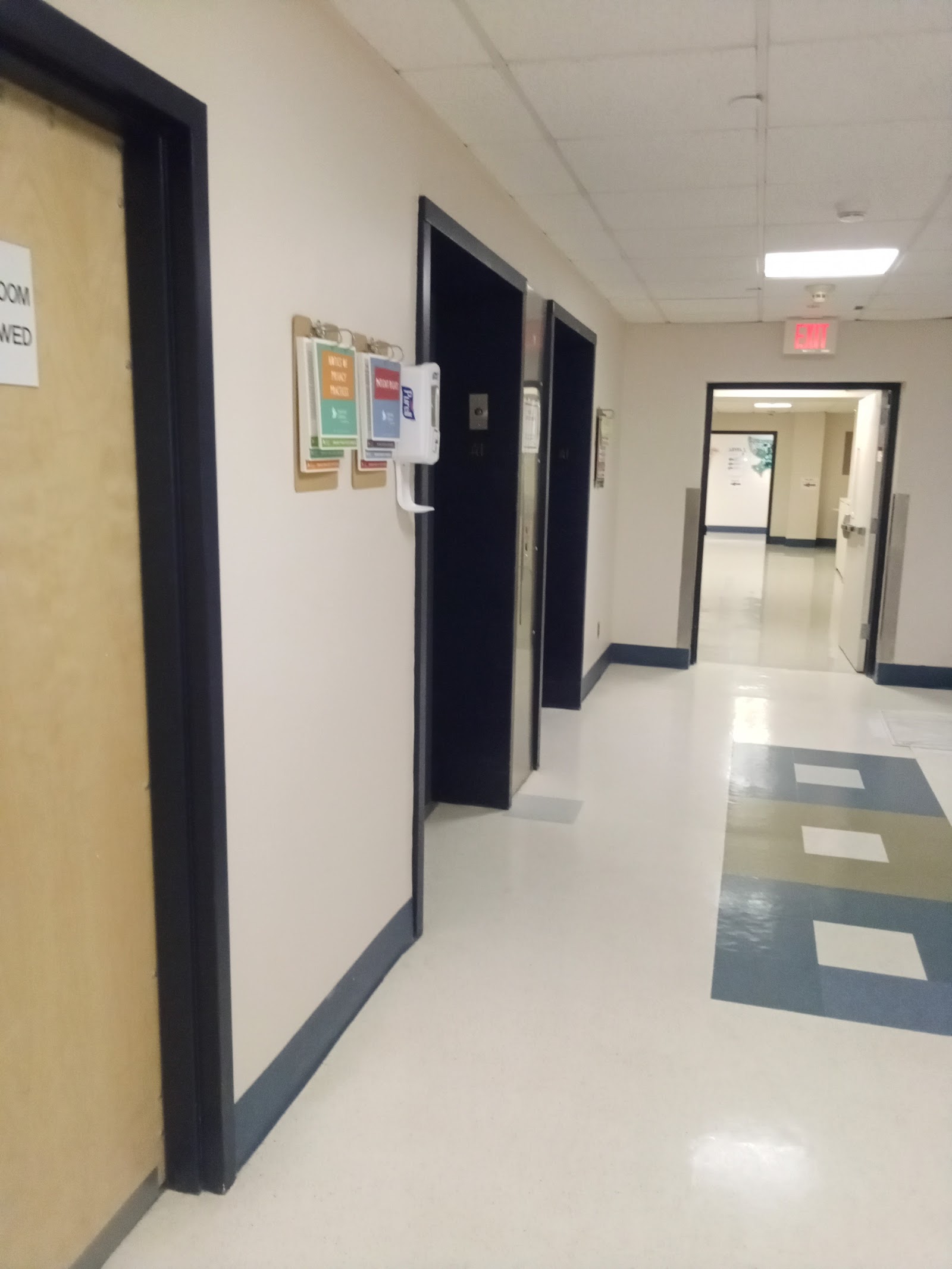 Interior hallway with clean floors, colored door frames, exit signage, and directional information boards