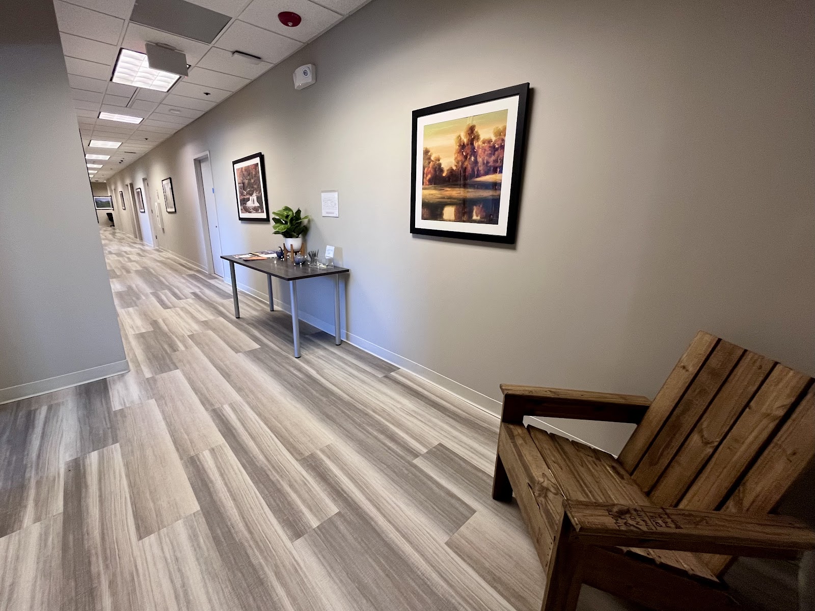 Interior corridor hallway with framed landscape artwork on walls, hardwood flooring, and natural lighting
