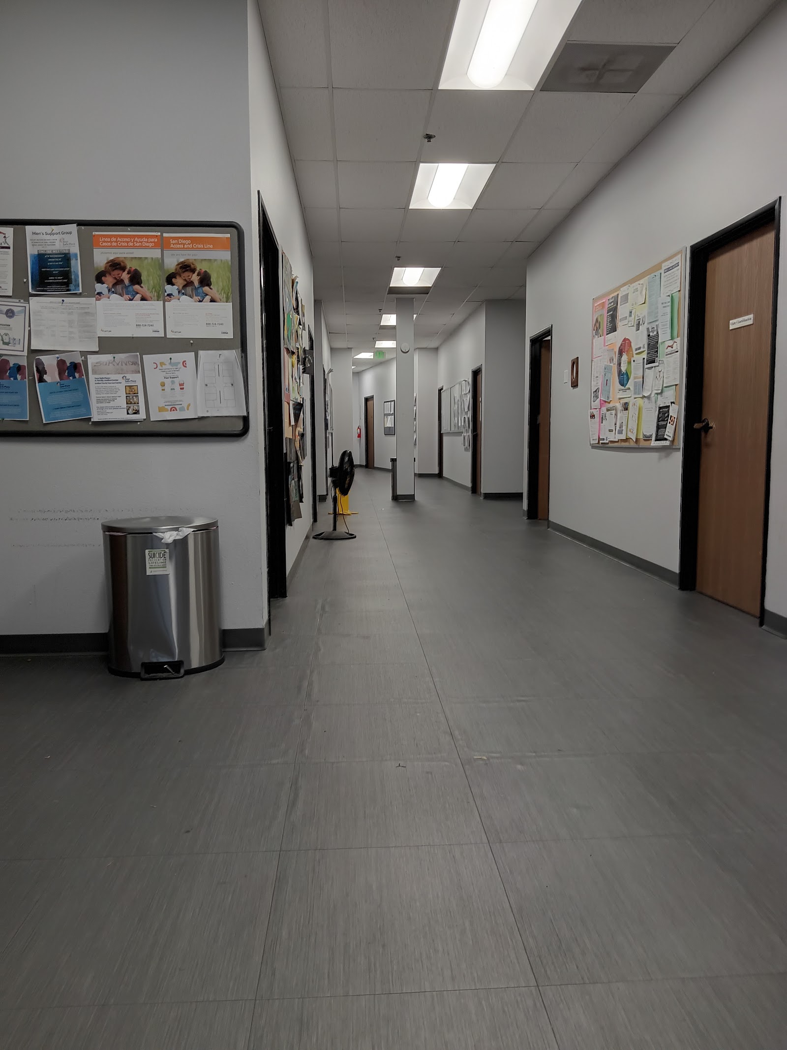 Interior hallway with educational posters, bulletin boards, trash receptacle, and doorways leading to treatment areas