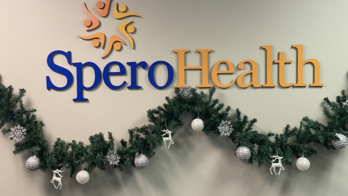 Interior wall featuring Spero Health logo, orange and blue company branding graphics, and seasonal holiday decorations