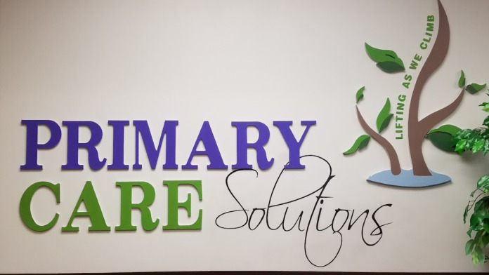 Interior wall displaying Primary Care Solutions logo and tagline with decorative tree graphic and green leaf accents