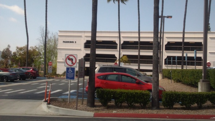 Exterior parking structure with marked spaces, palm trees, landscaping and facility grounds approach