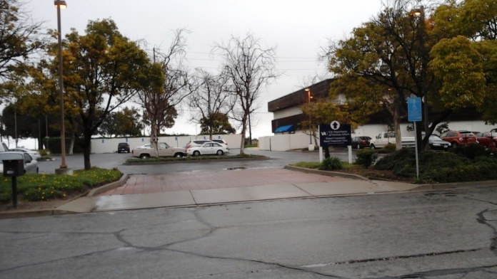 Exterior parking lot view of VA clinic building with landscaping, vehicles, and street signage