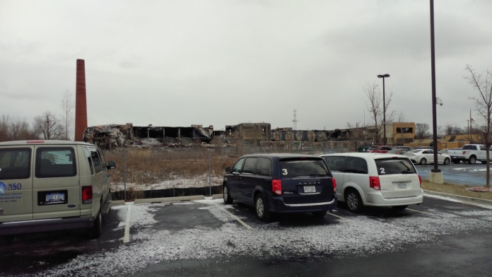 Exterior parking lot with service vehicles and building grounds, industrial area visible in background