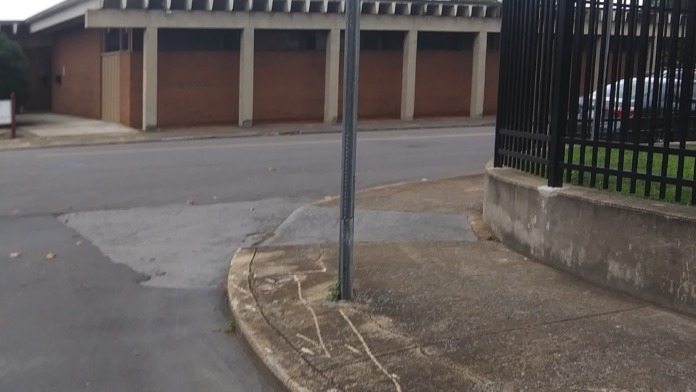 Exterior view of facility parking area with security fence, brick building structure, and tree-lined street access