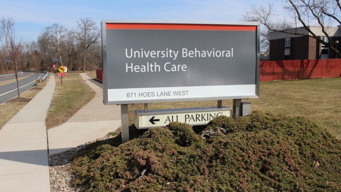Exterior directional sign reading University Behavioral Health Care at 671 Hoes Lane West with landscaping and property entrance visible