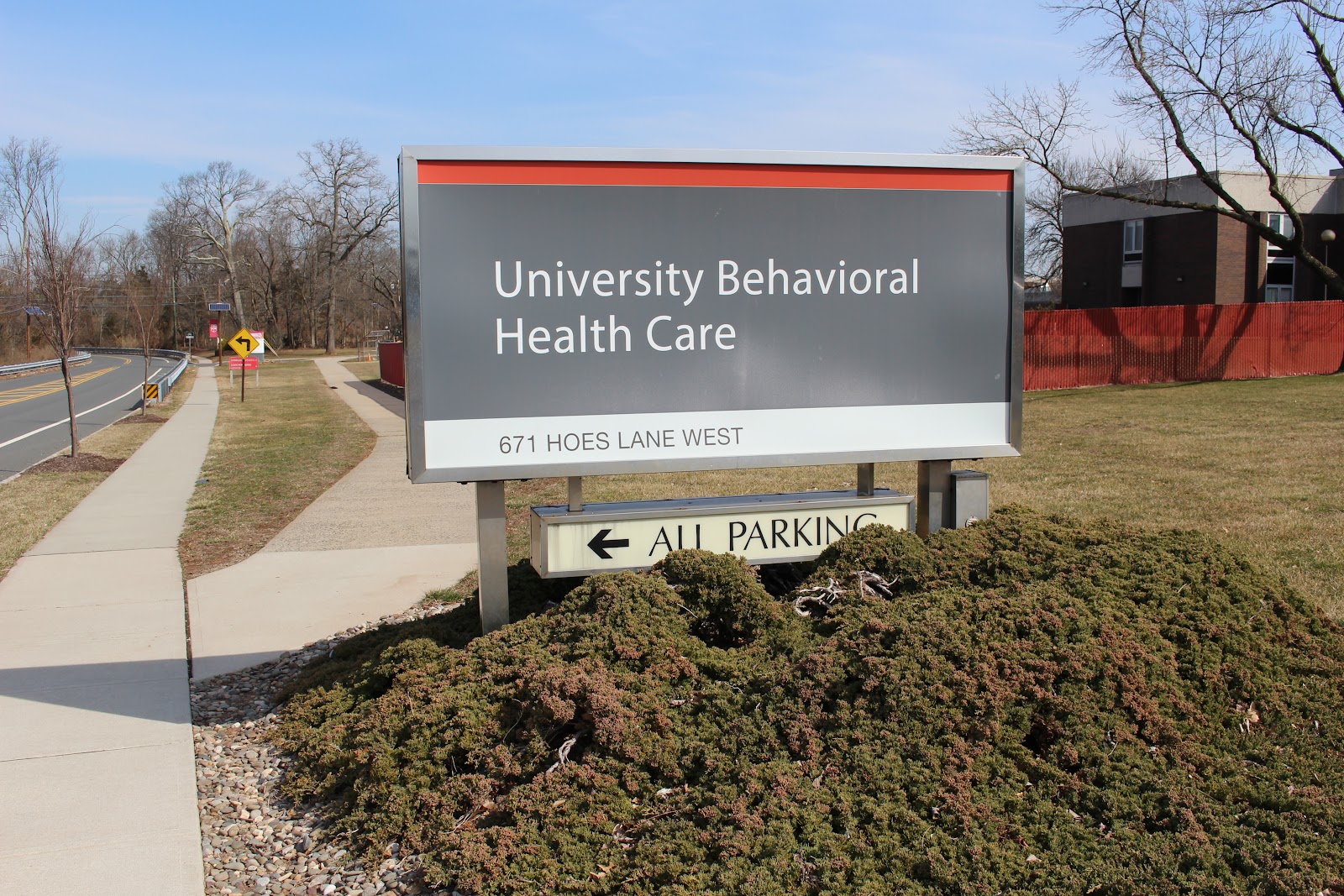 Exterior directional sign reading University Behavioral Health Care at 671 Hoes Lane West with landscaping and property entrance visible