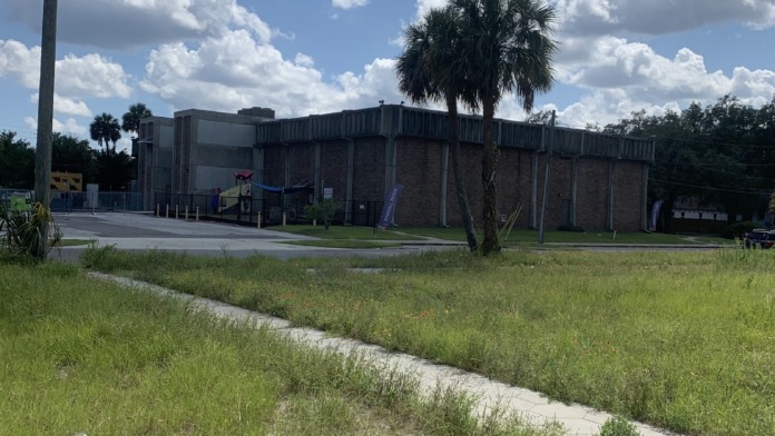 Exterior side view showing brick construction, parking area, mature palm trees, and utility poles