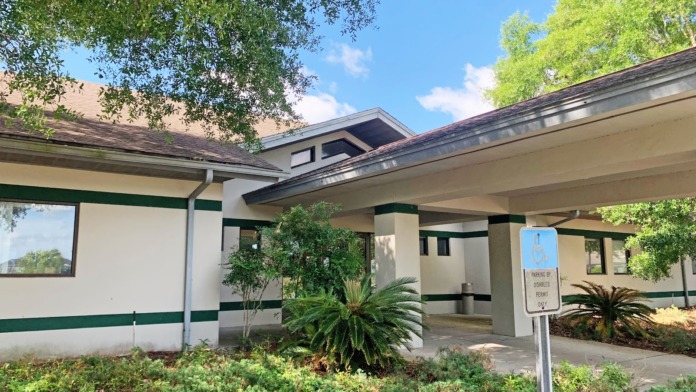 Exterior showing covered walkway with green and white trim, mature landscaping, and accessible parking area
