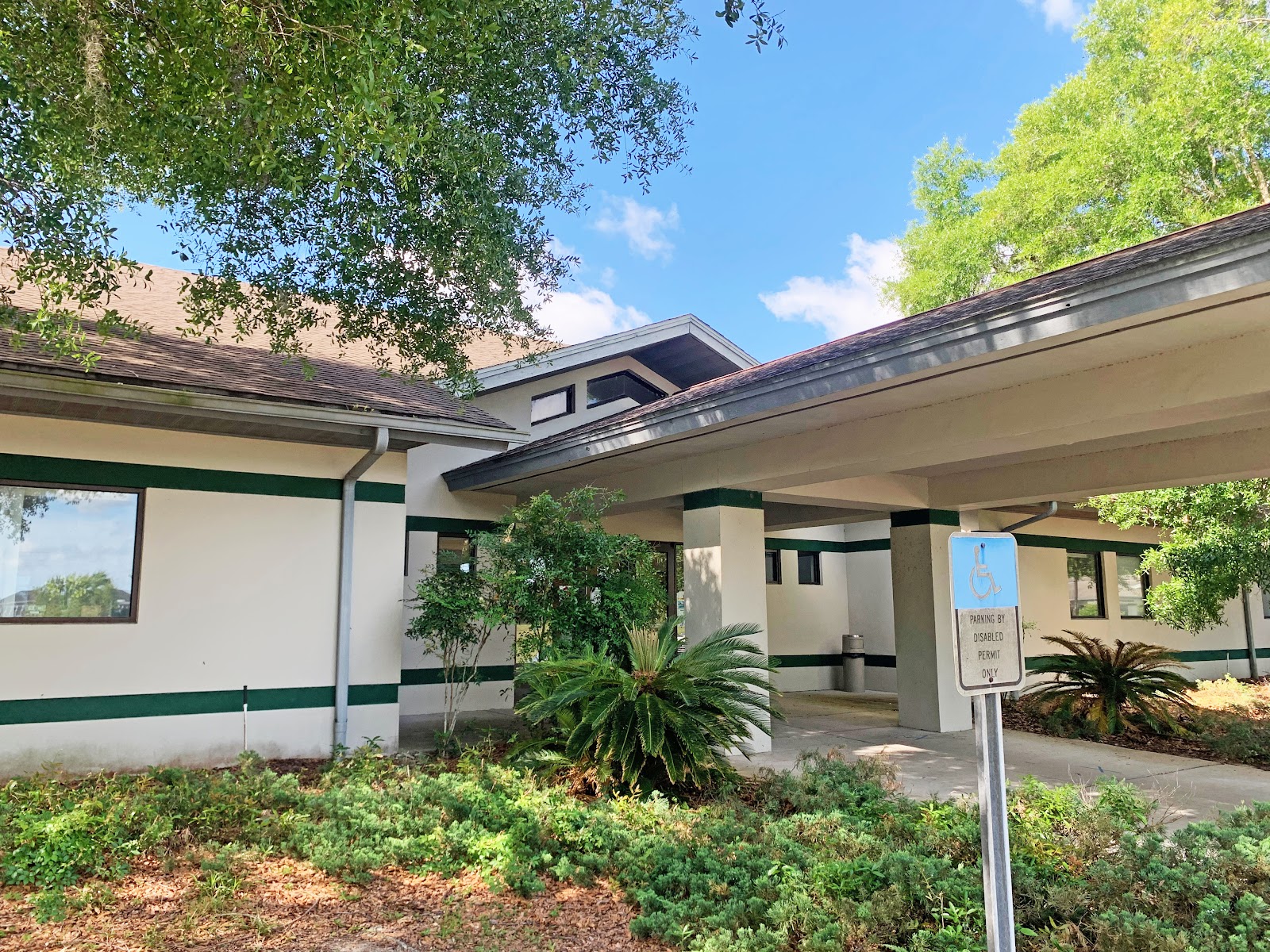 Exterior showing covered walkway with green and white trim, mature landscaping, and accessible parking area