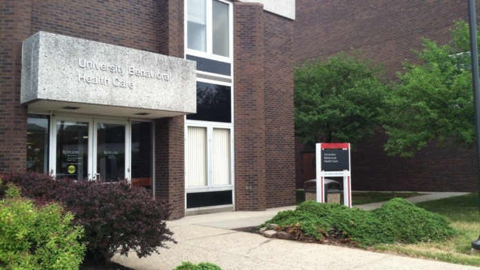 Exterior side entrance of brick building with white trim windows, green shrub landscaping, and facility signage visible