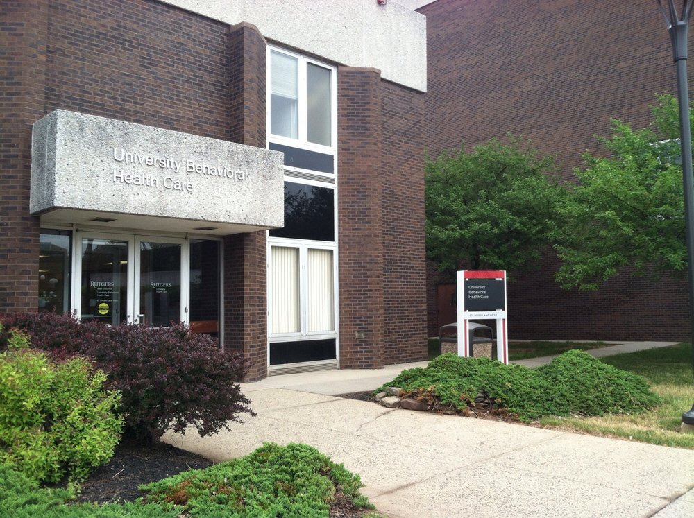 Exterior side entrance of brick building with white trim windows, green shrub landscaping, and facility signage visible