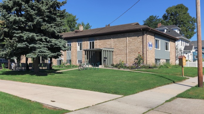 Exterior street view showing brick facility building with large landscaped lawn, mature trees, and residential neighborhood.