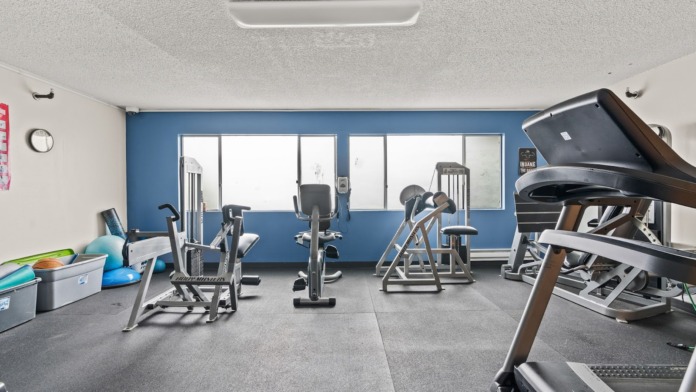 Interior fitness center with exercise equipment including treadmills, stationary bikes, blue accent wall, and large windows