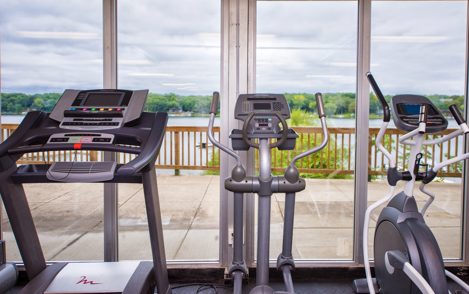 Interior fitness center featuring treadmill, elliptical machine, stationary bike and panoramic lake windows