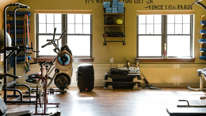 Interior fitness facility with stationary bikes, exercise equipment, motivational wall quote, and large windows with natural light