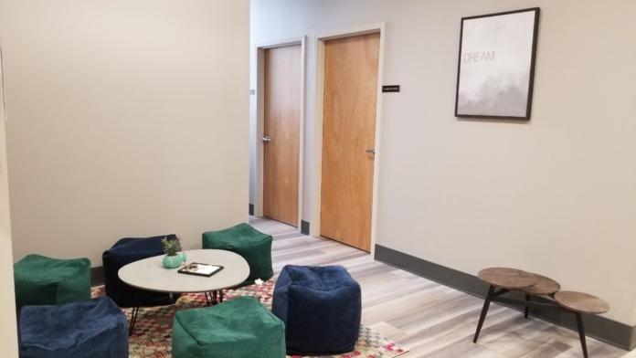 Interior common area with green and blue bean bag seating, round white table, wooden side tables, and inspirational wall art