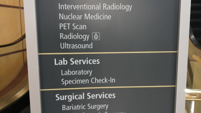 Interior directional sign showing escalator location and medical services including imaging and surgical services