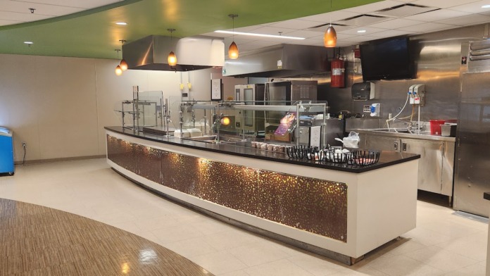 Interior commercial kitchen with stainless steel equipment, serving counters, pendant lighting, and modern food preparation area