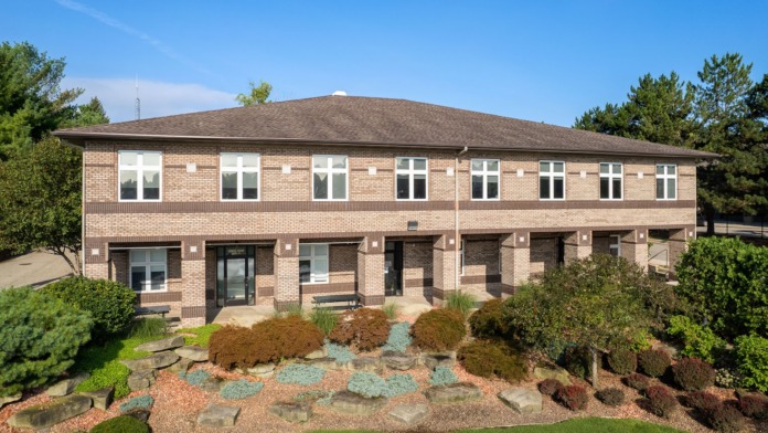 Multi-story brick building exterior with entrance doors, decorative landscaping, and manicured grounds